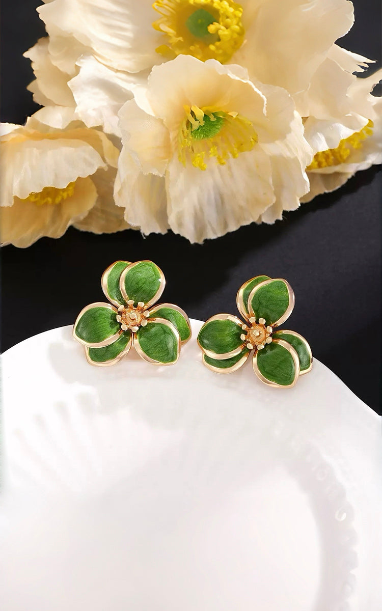 Green floral earrings on a white surface with flowers in the background