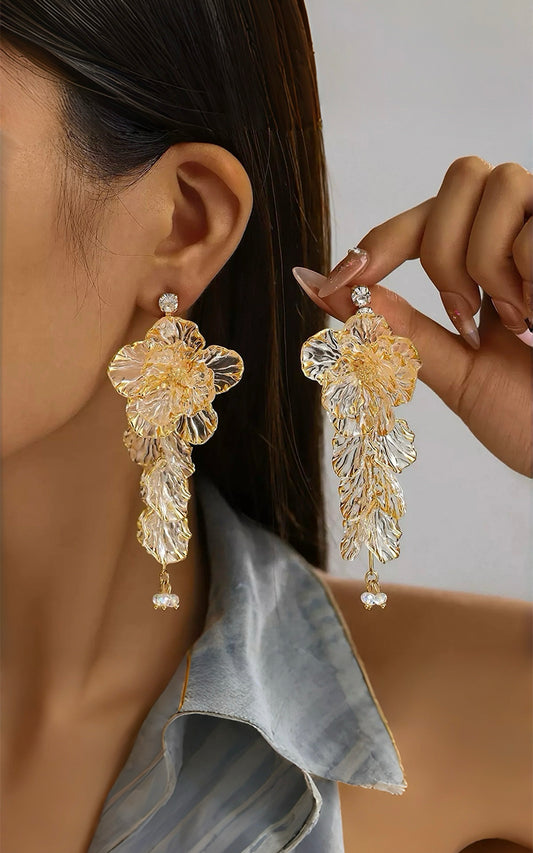 Close-up of a person wearing champagne floral earrings with a neutral background
