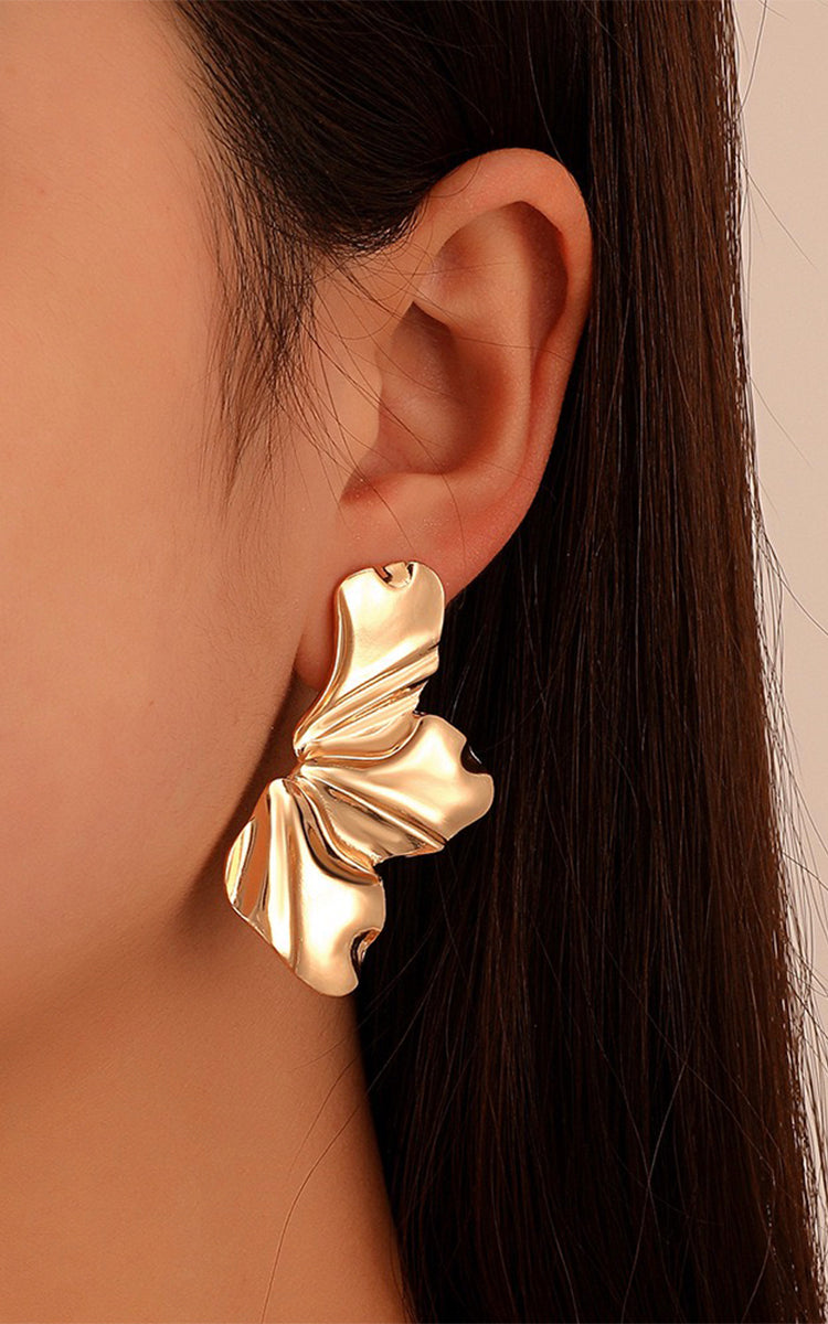 Gold leaf-shaped earring worn by a person with long dark hair.