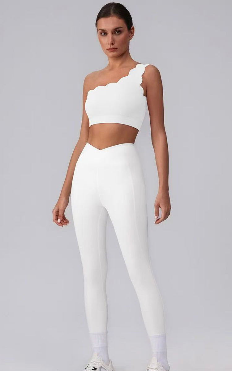 Woman wearing a white one-shoulder top and leggings on a gray background