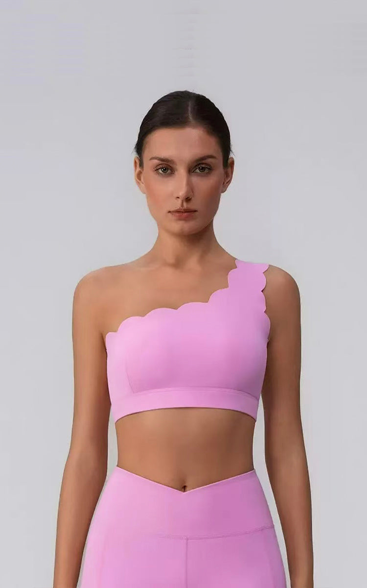 Model wearing a pink one-shoulder top and legging against a gray background