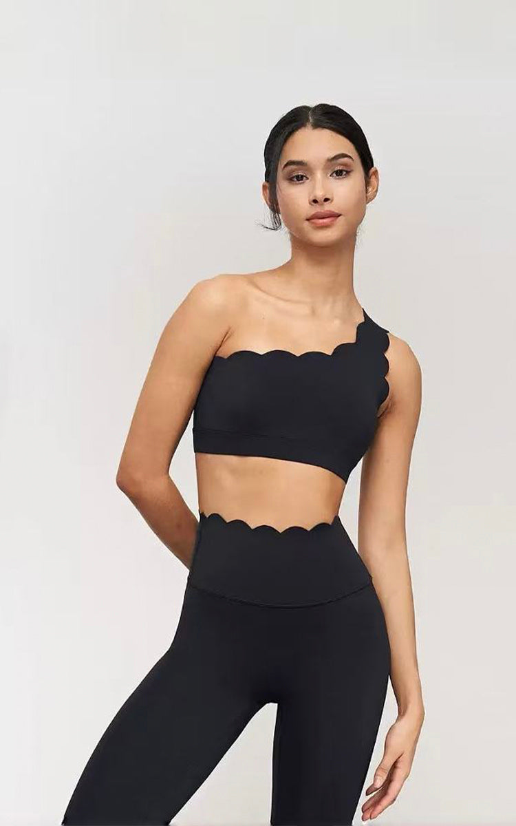 Woman wearing a black scalloped sports bra and leggings on a white background