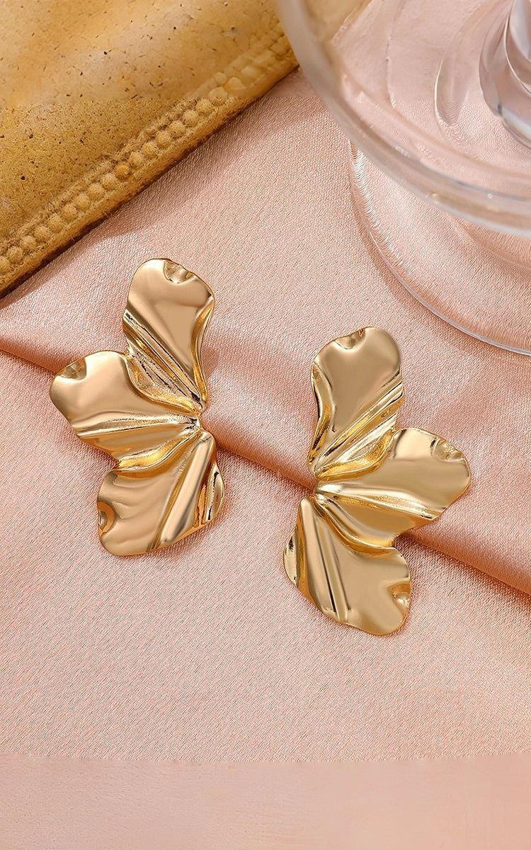 Gold butterfly earrings on a pink surface