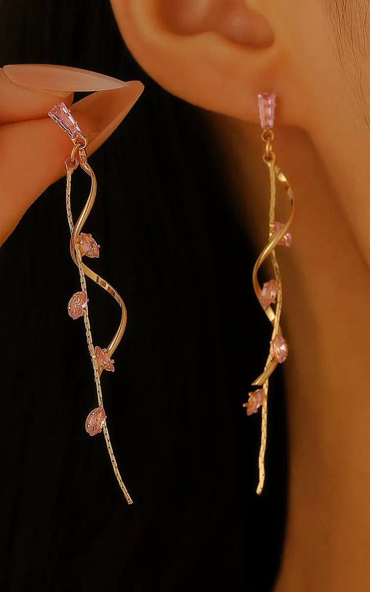 Gold earrings with pink gemstones worn by a person against a dark background