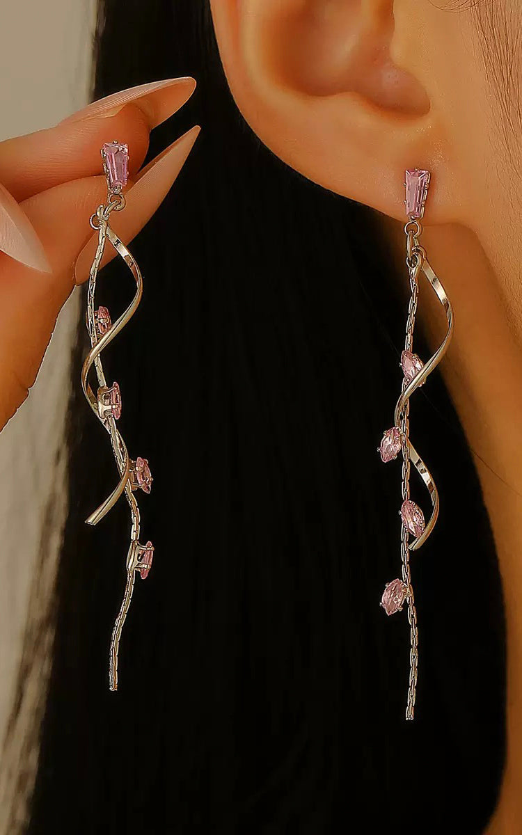 Silver earrings with pink gemstones being held near an ear against a dark background
