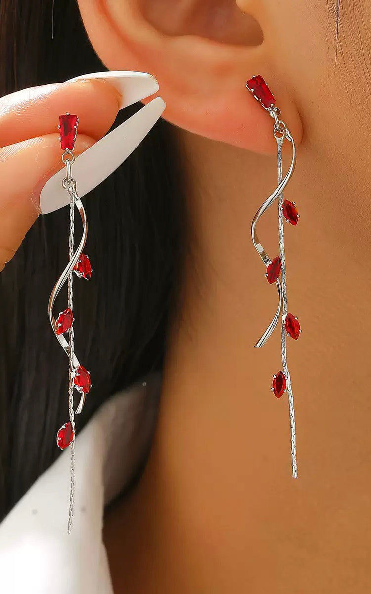 Silver earrings with red stones worn by a person against a neutral background
