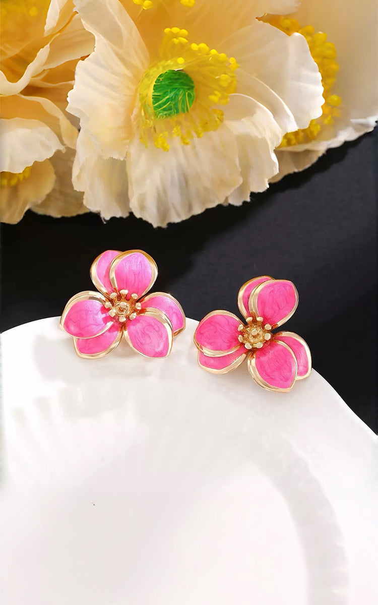 Pink flower-shaped earrings on a white surface with a yellow flower in the background