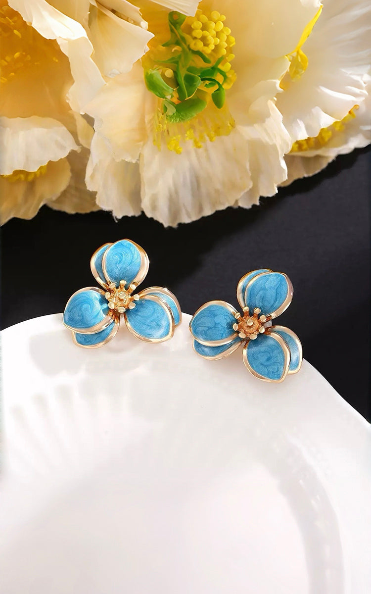 Blue flower-shaped earrings on a white surface with a black background