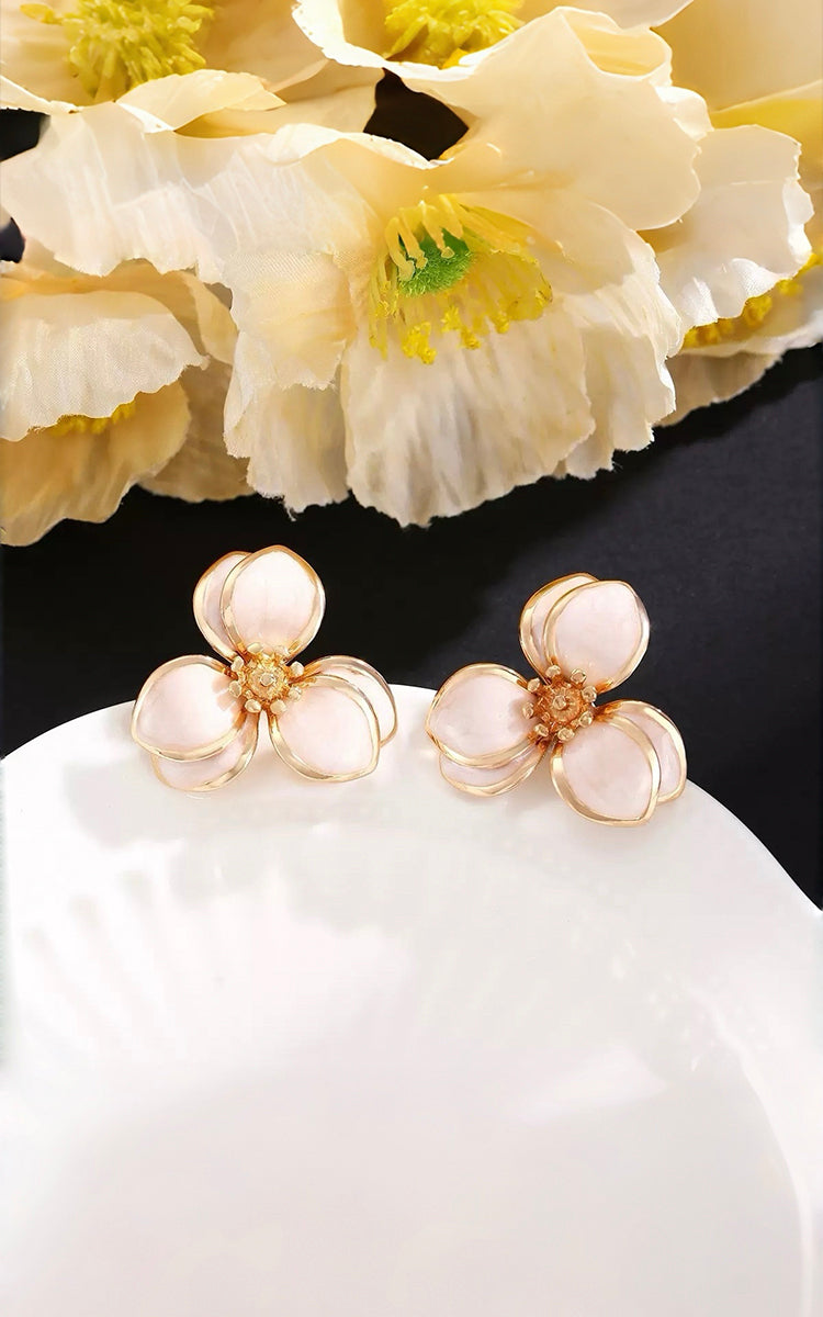 Pair of floral earrings on a white surface with flowers in the background