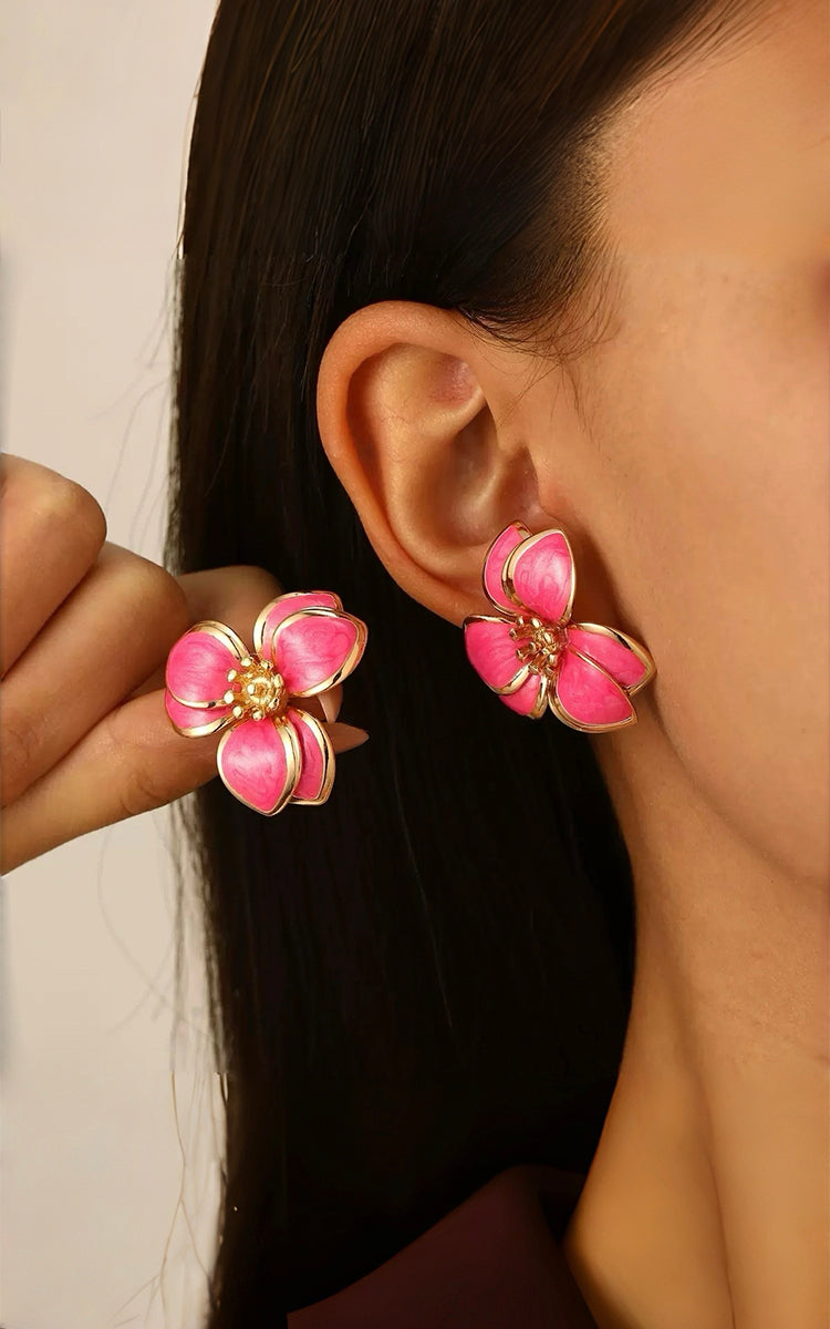 Close-up of a person wearing pink floral earrings with yellow accents.